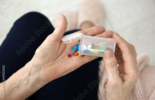 Elderly woman holding container and different pills, closeup