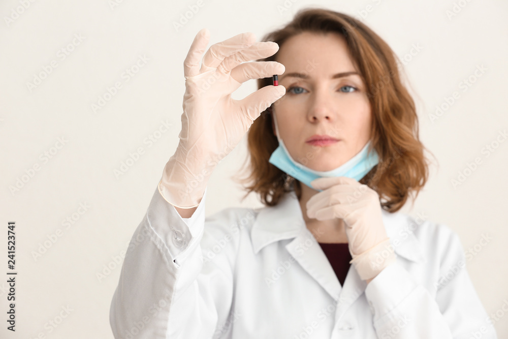 Young doctor holding pill on light background Young doctor holding pill on light background