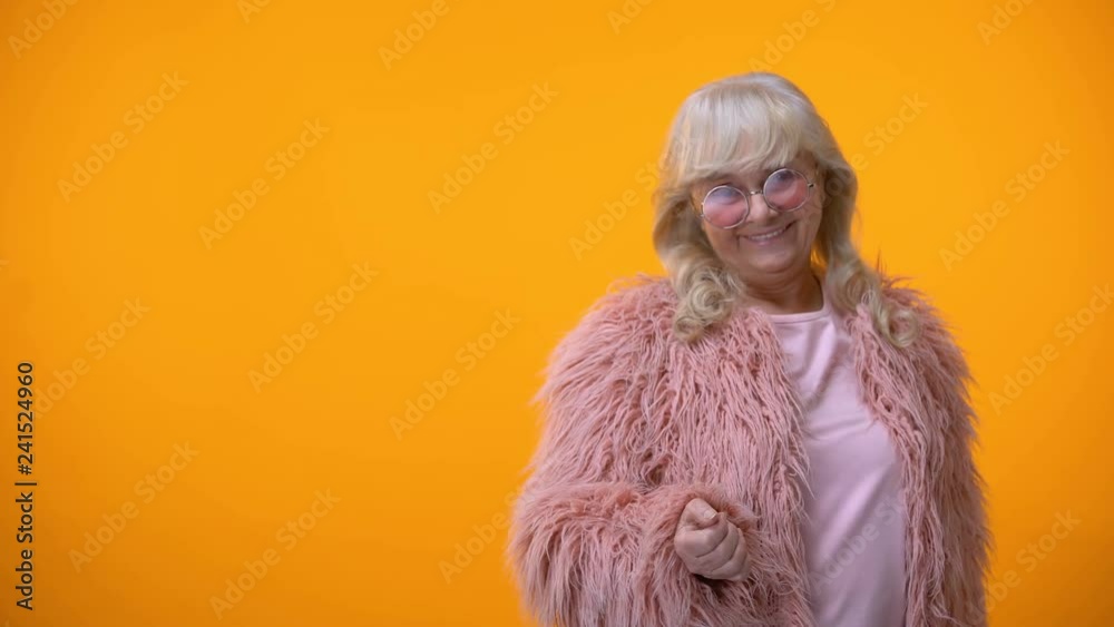 Cheerful retiree lady in funny pink coat and round sunglasses sending air kiss Cheerful retiree lady in funny pink coat and round sunglasses sending air kiss