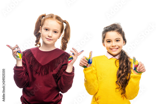 cute schoolgirls smiling, showing hands painted in colorful paints and looking at camera isolated on white