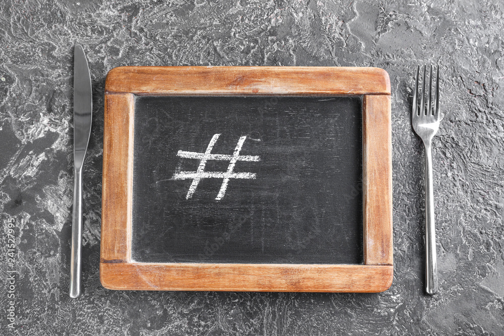 Chalkboard with drawn hashtag symbol, knife and fork on grey background
