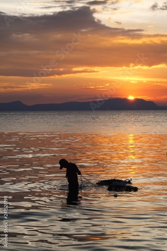 silhouette of boy pulling the crab cages on the shore at sunset