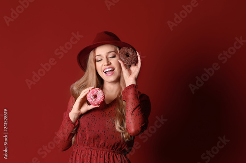 Beautiful young woman with tasty donuts on color background