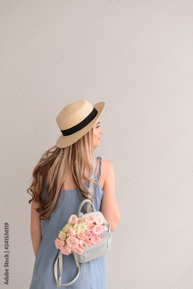 Beautiful young woman with bouquet of flowers and backpack on grey background Beautiful young woman with bouquet of flowers and backpack on grey background