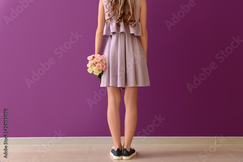 Beautiful young woman with bouquet of flowers near color wall, back view