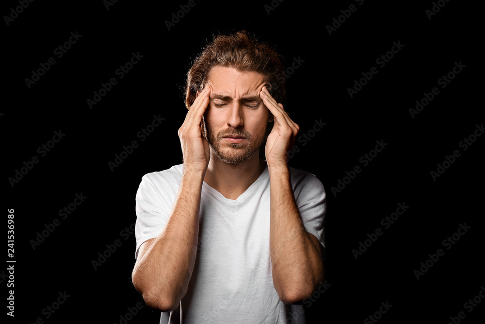 Young man suffering from headache on dark background Young man suffering from headache on dark background