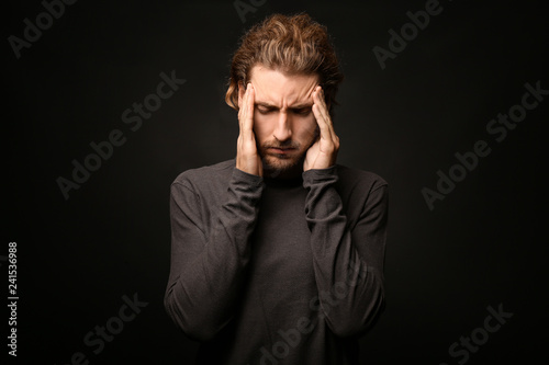 Young man suffering from headache on dark background © Pixel-Shot