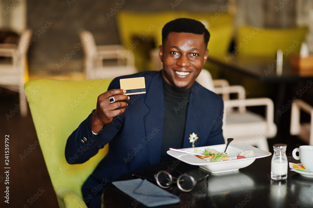 Fashionable african american man in suit sitting at cafe with credit card in his hand.