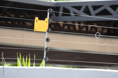 high voltage security fence on house wall with blank yellow plastice sign. photo