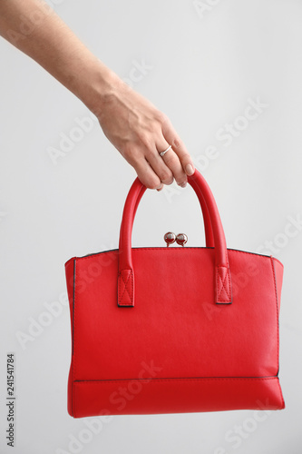 Female hand with stylish bag on light background