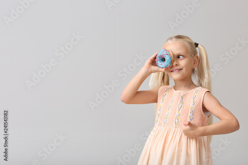 Cute little girl with donut on light background