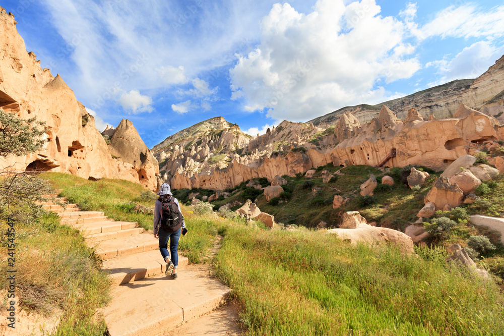 A young woman with a backpack on her back walks between huge and old stones in the Cappadocian honey valley.