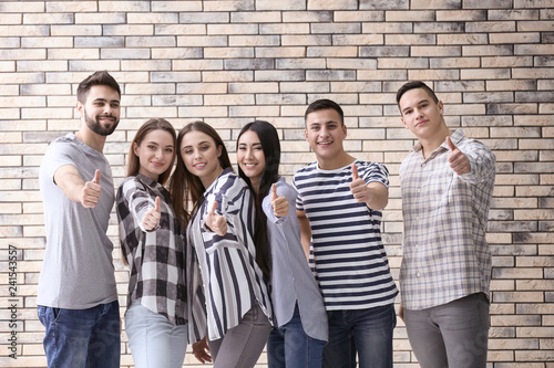 Young people showing thumb-up gesture on brick background