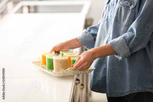 Woman holding tray with different tasty smoothies in kitchen