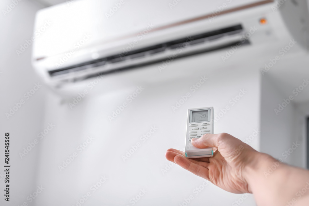 Young man switching on air conditioner indoors, closeup