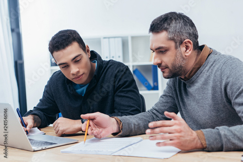 concentrated male coworkers working with papers and laptop in office photo