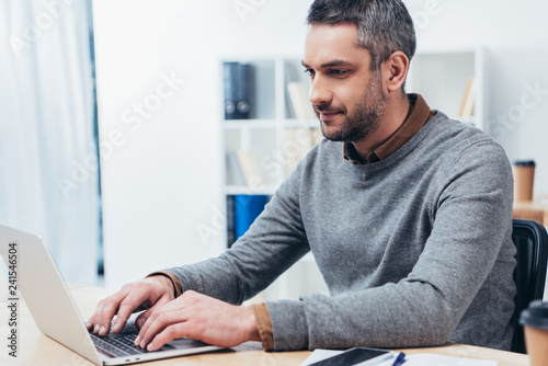 handsome smiling bearded businessman working with laptop in office