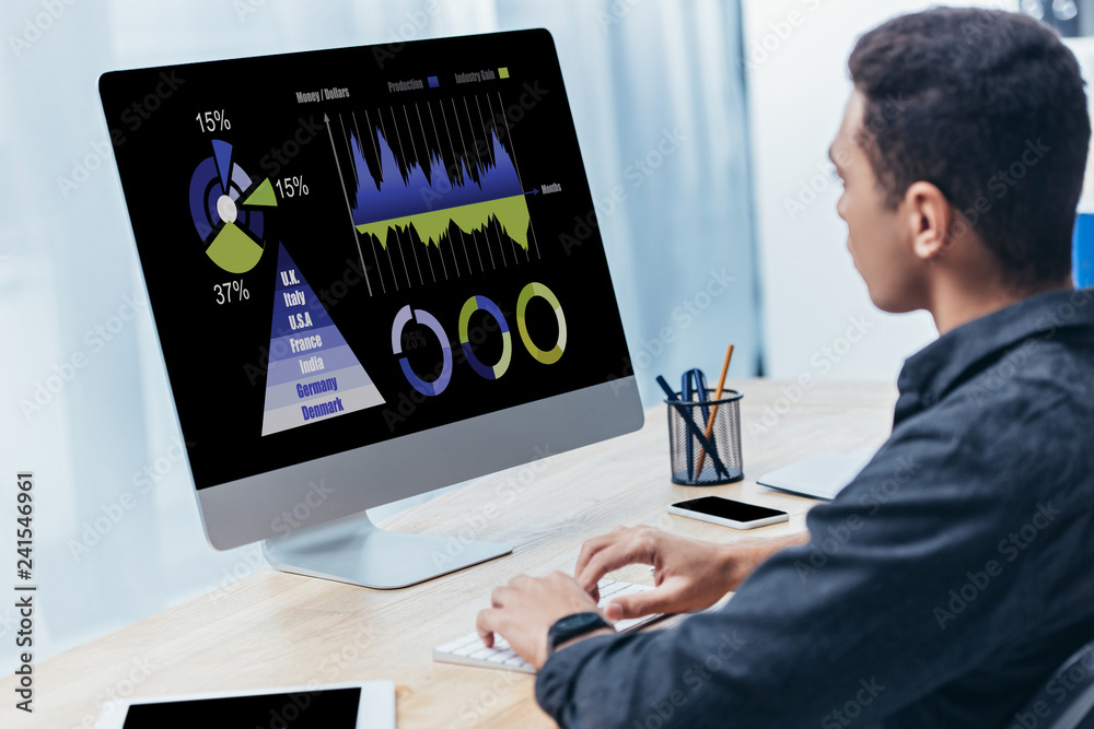 Obraz premium young businessman using desktop computer with business charts on screen in office