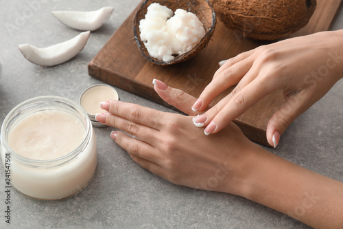 Woman applying coconut oil onto skin on grey background photo