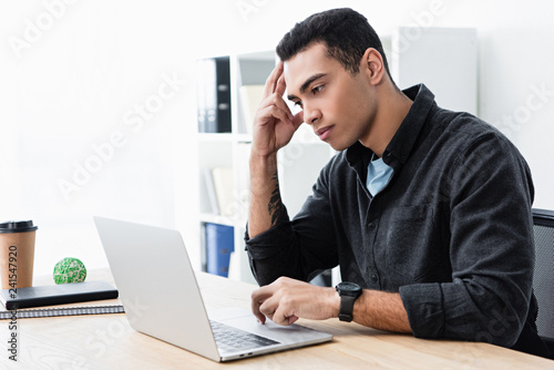 serious concentrated young businessman working with laptop in office