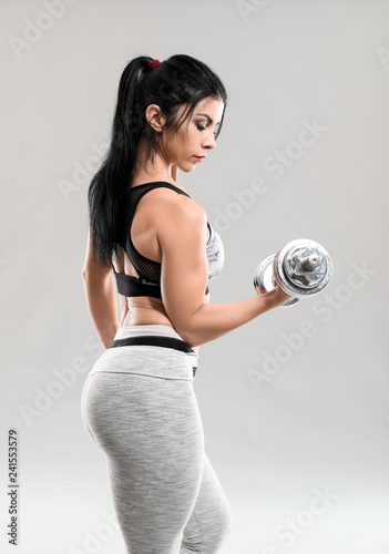 Sporty muscular woman with dumbbell on grey background