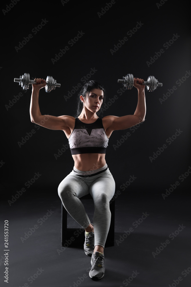 Sporty muscular woman with dumbbells on dark background Sporty muscular woman with dumbbells on dark background