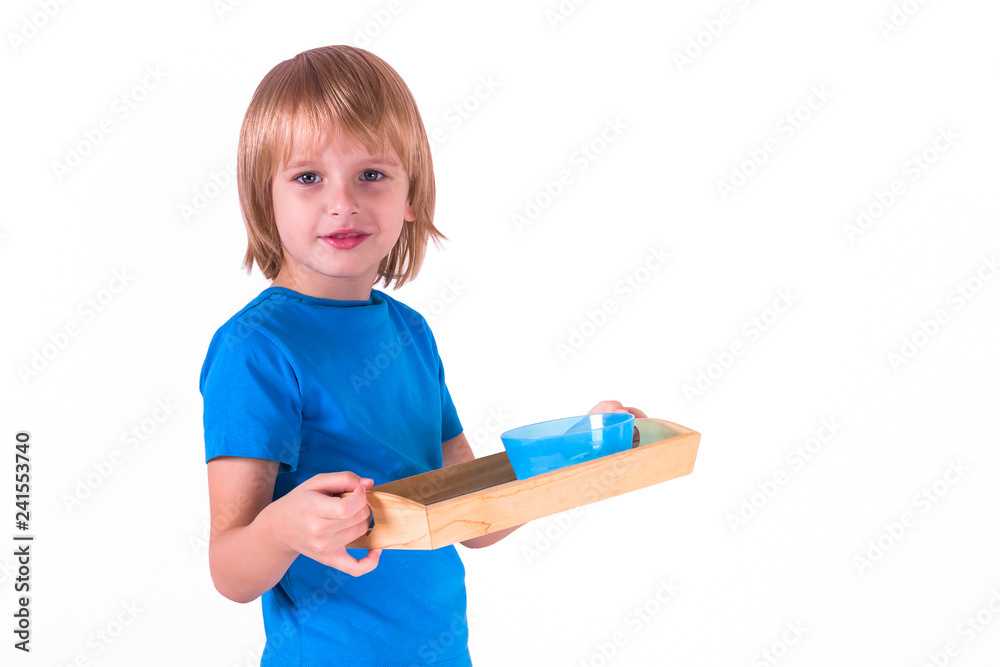 Toddler boy standing with a tray of Montessori materials for a lesson of practical life on a white background, isolate. Exercise cutting with scissors. Toddler boy standing with a tray of Montessori materials for a lesson of practical life on a white background, isolate. Exercise cutting with scissors.