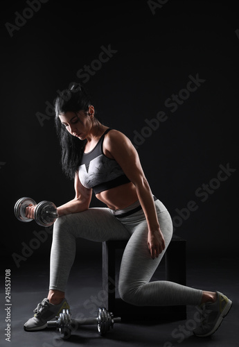 Sporty muscular woman with dumbbell on dark background