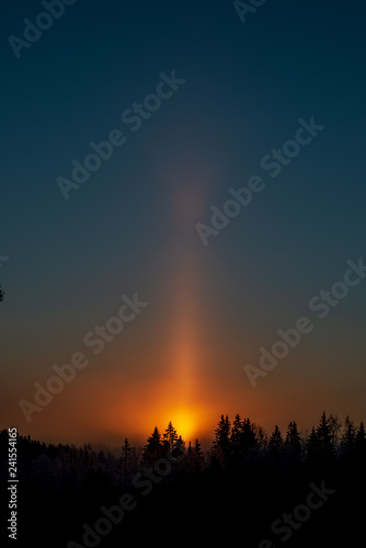 cold sunrise in winter forest with sun light pillar