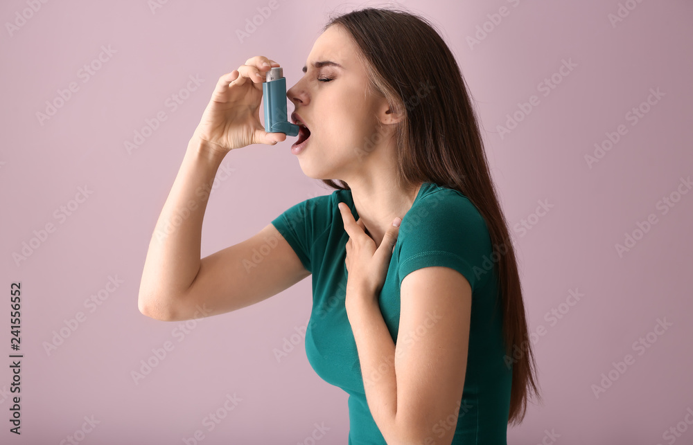 Young woman with inhaler having asthma attack on color background Young woman with inhaler having asthma attack on color background