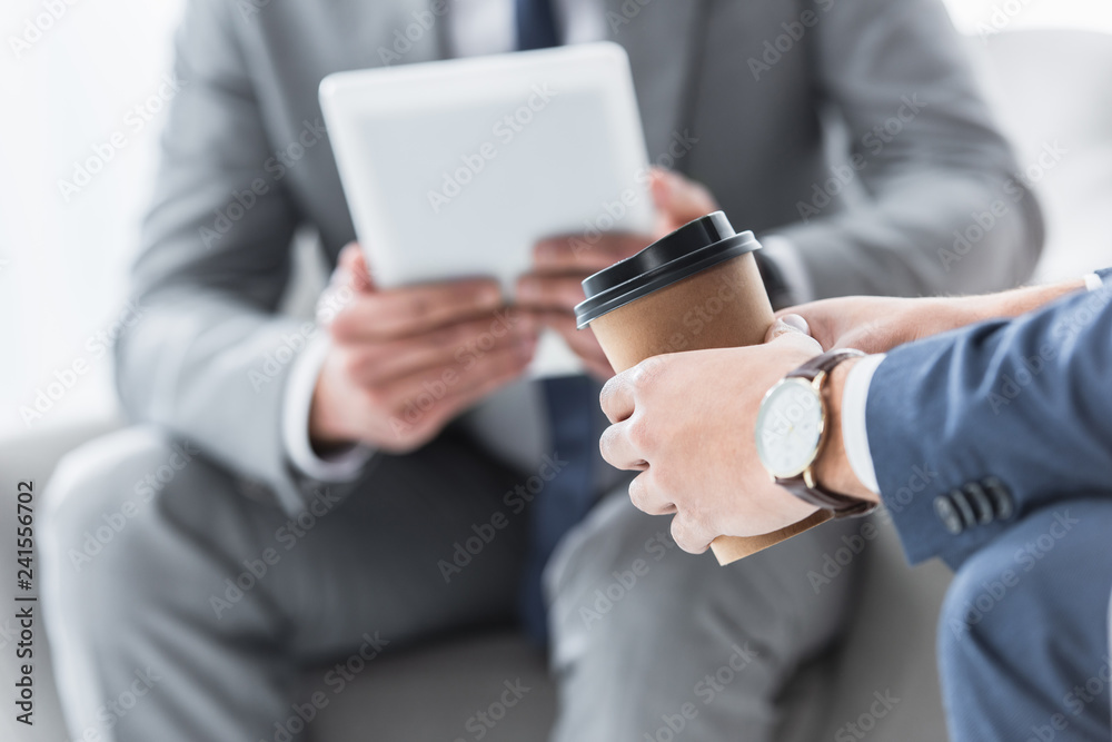 cropped shot of businessman holding coffee to go and colleague using digital tablet behind cropped shot of businessman holding coffee to go and colleague using digital tablet behind