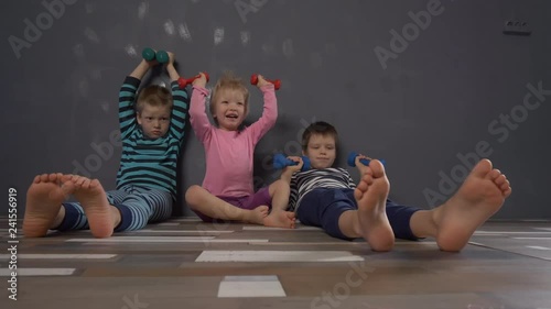 Cheerful children in multi-colored striped clothes are engaged in gymnastics with dumbbells. Legs and feet close-up. Children enjoy winter vacations together. Concept of family fitness classes.