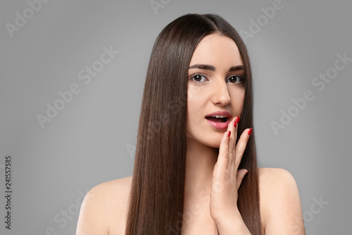 Portrait of young woman with beautiful straight hair on grey background