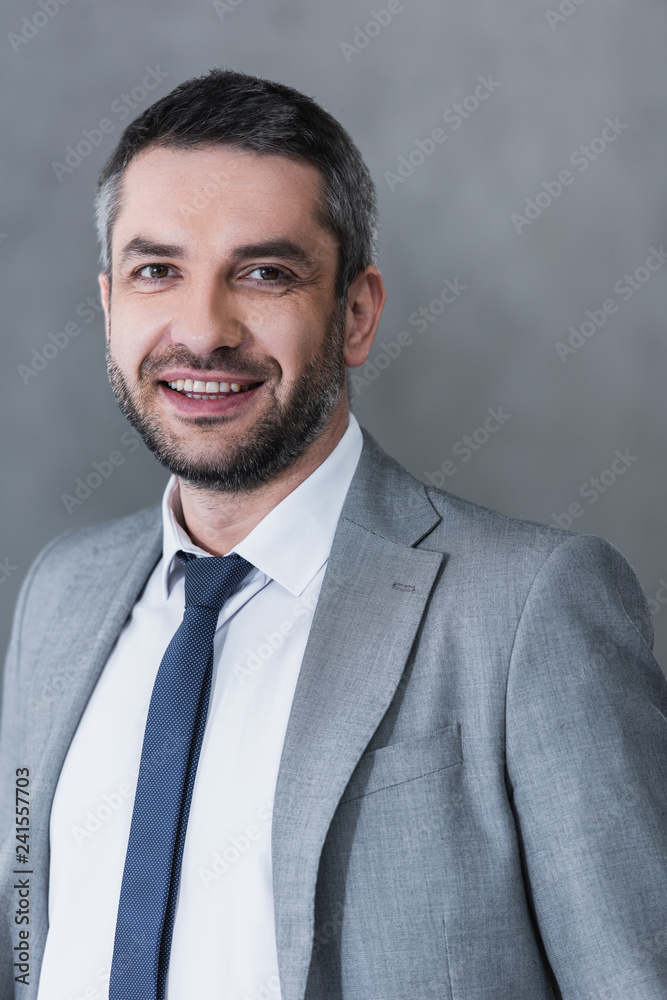 handsome happy businessman in formal wear smiling at camera on grey handsome happy businessman in formal wear smiling at camera on grey