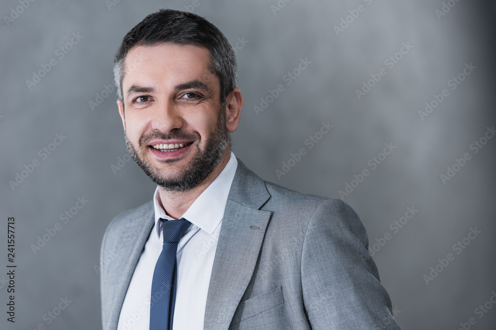 portrait of handsome businessman in formal wear smiling at camera on grey portrait of handsome businessman in formal wear smiling at camera on grey