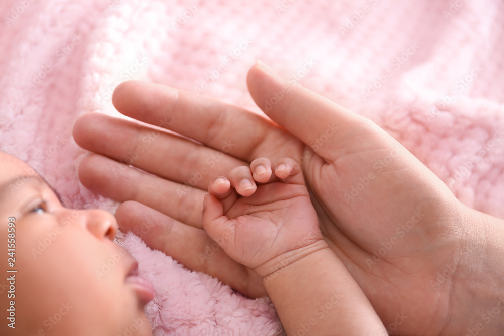 Cute African-American baby with mother's hand on soft plaid, closeup Cute African-American baby with mother's hand on soft plaid, closeup