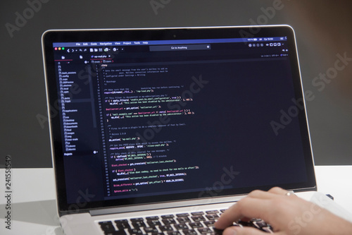 Male programmer working on laptop computer at white desk in office