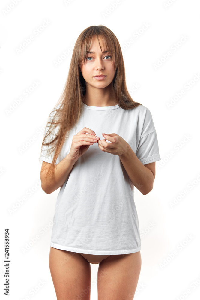 Attractive young woman in oversized white t-shirt, being in underwear, shows perfect slim body and healthy skin, posing over white studio background. Attractive young woman in oversized white t-shirt, being in underwear, shows perfect slim body and healthy skin, posing over white studio background.