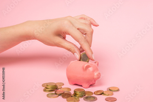 Fotografie Female hand inserting a one euro coin into a pink ceramic piggy bank