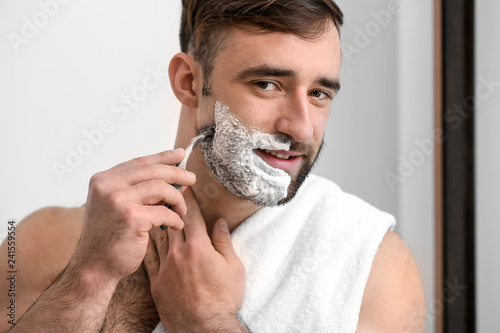 Handsome man shaving in bat...
