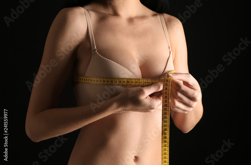 Young woman measuring her breast on dark background