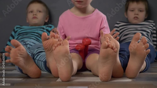 Cheerful children in multi-colored striped clothes are engaged in gymnastics with dumbbells. Legs and feet close-up. Children enjoy winter vacations together. Concept of family fitness classes.