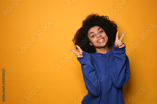 Portrait of young African-American woman showing victory gesture on color background © Pixel-Shot