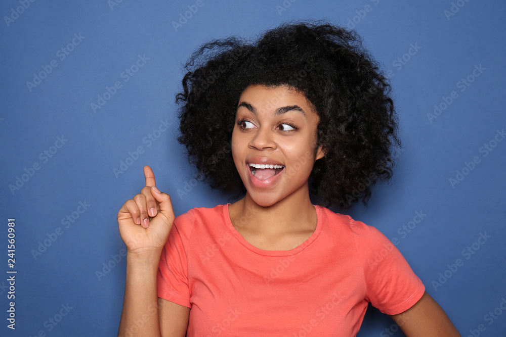 Portrait of young African-American woman with raised index finger on color background