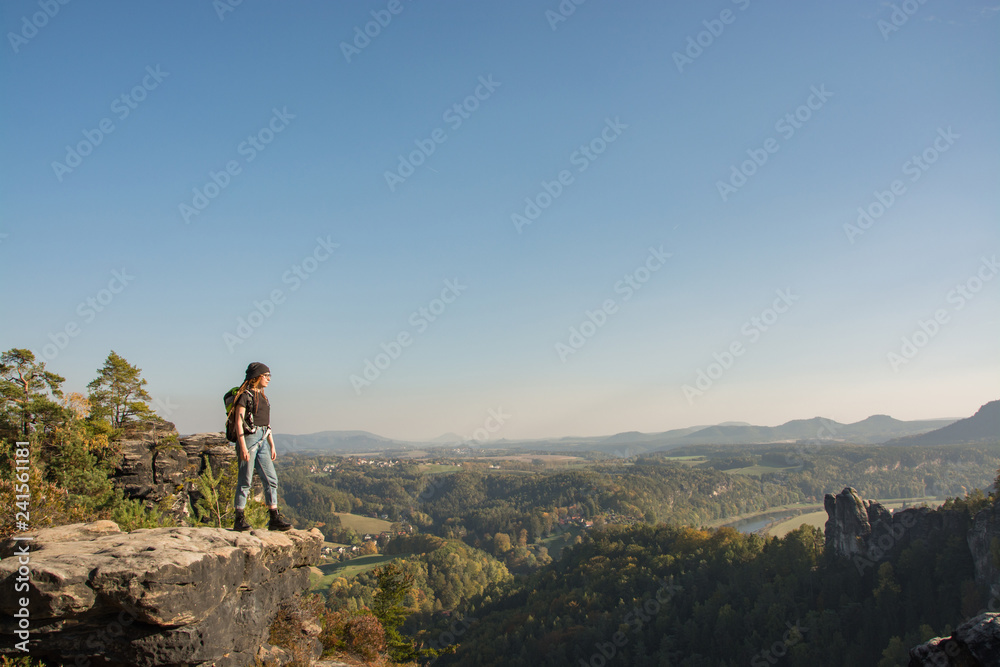 Young woman traveler with baclpack stand on the cliff in mountains