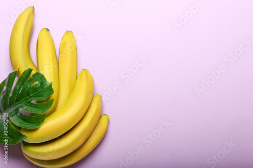 Ripe sweet bananas and tropical leaf on color background © Pixel-Shot