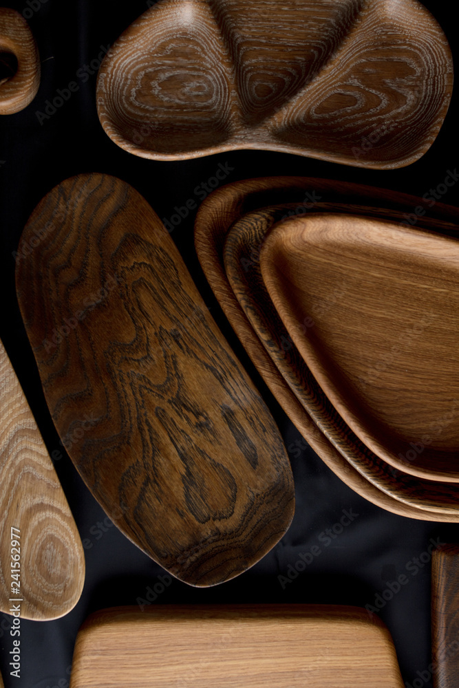 Top view of unused brand new brown handmade wooden kitchen utensil, made from different wood species, dish plate and cutting board on black background Top view of unused brand new brown handmade wooden kitchen utensil, made from different wood species, dish plate and cutting board on black background