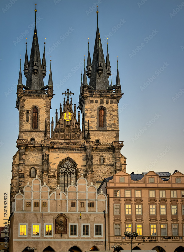 Fototapeta premium Church of Our Lady before Týn, an ornate gothic medieval catholic church with towers and spires, behind cafes in the Old Town Square, Prague, Czech Republic with golden sunset reflected in the windows