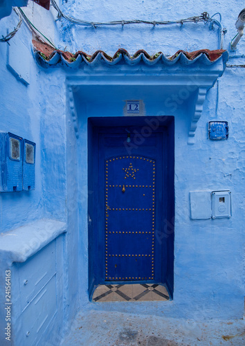 Typical, old, blue intricately carved, studded, Moroccan riad door and door-frame and old house. Beautiful view of the blue city in the medina. painted houses in CHEFCHAOUEN, MOROCCO © mitzo_bs