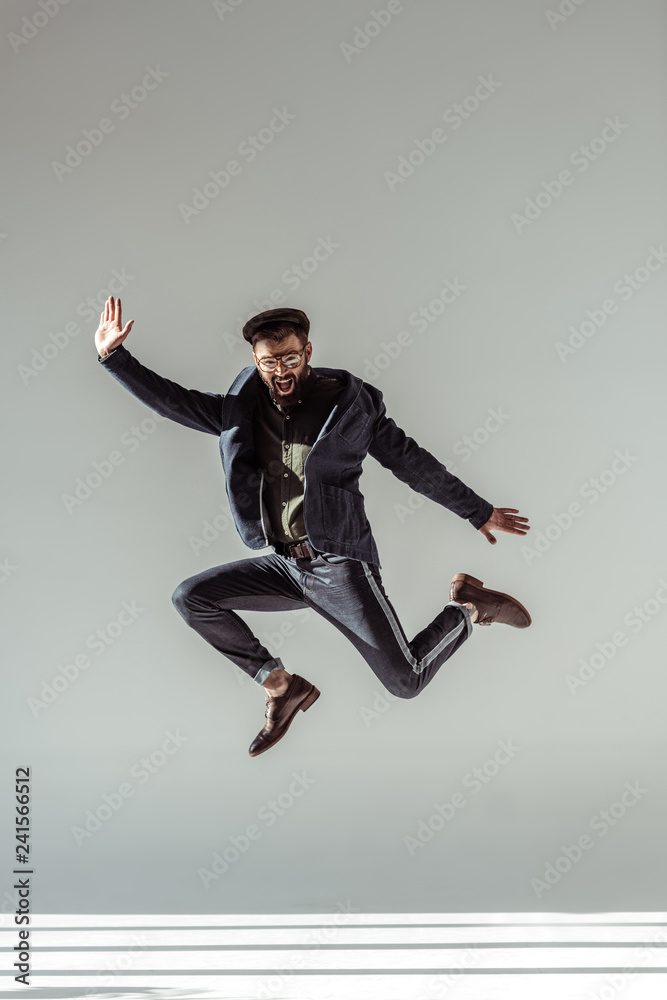 handsome man in cap and glasses jumping on grey background